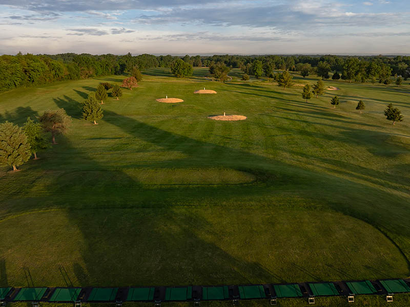 Practice area at Flatbush Golf Course in Littlestown, Pennsylvania, featuring driving range hitting bays, target greens, open turf, trees, and rolling course views.