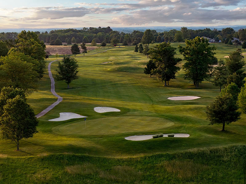 Hole 1 at Flatbush Golf Course in Littlestown, Pennsylvania, featuring a wide fairway, green-side sand bunkers, tree-lined views, and rolling countryside.
