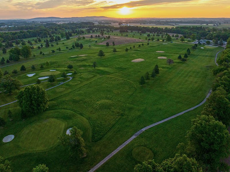 Aerial sunset view of Flatbush Golf Course in Littlestown, Pennsylvania, showing rolling fairways, sand bunkers, cart paths, trees, and surrounding countryside.