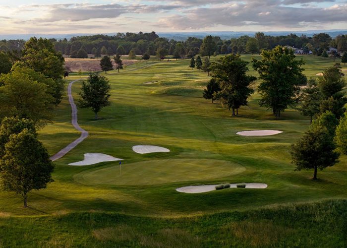Hole 1 at Flatbush Golf Course in Littlestown, Pennsylvania, featuring a wide fairway, green-side sand bunkers, tree-lined views, and rolling countryside.